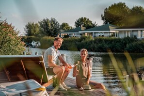 Una pareja descansando en un muelle junto a un cuerpo de agua, con una casa al fondo.