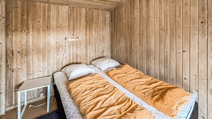 A single bed with a white mattress and orange bedding in a room with wooden walls and a small bedside table. - 3 bedroom nice home in Skjern (Skjern)