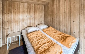 A single bed with a white mattress and orange bedding in a room with wooden walls and a small bedside table. - 3 bedroom nice home in Skjern (Skjern)
