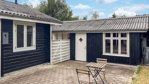 A building with a dark exterior, a white door, and a window. There is a small table and a bench in the foreground. - 3 bedroom nice home in Skjern (Skjern)