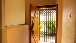 Une porte en bois avec un portail en métal, une vue sur la verdure à l’extérieur et un interrupteur sur le mur.