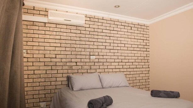 Une chambre d’hôtel avec une tête de lit décorée d’un motif en briques, un lit avec deux oreillers et une serviette roulée posée sur le lit.
