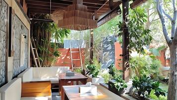 An outdoor seating area with a wooden table and benches, surrounded by greenery and a view of a building.