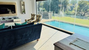 Un salon moderne doté d’un grand téléviseur, d’un canapé, d’un fauteuil et offrant une vue sur une piscine.