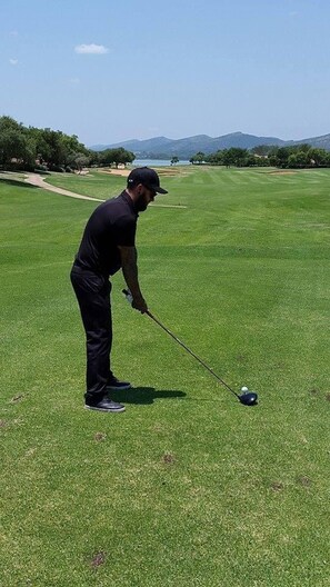 A person on a golf course with a clear sky and distant mountains.
