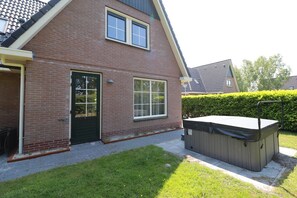 Een twee verdiepingen tellend, bakstenen huis met een voordeur, twee ramen en een hottub in de tuin.