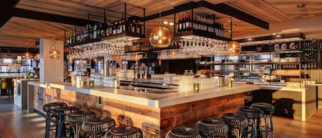 A bar area with a wooden ceiling, bar stools, and shelves stocked with bottles and glasses.