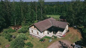 A two-story house with a sloped roof, surrounded by dense forest.