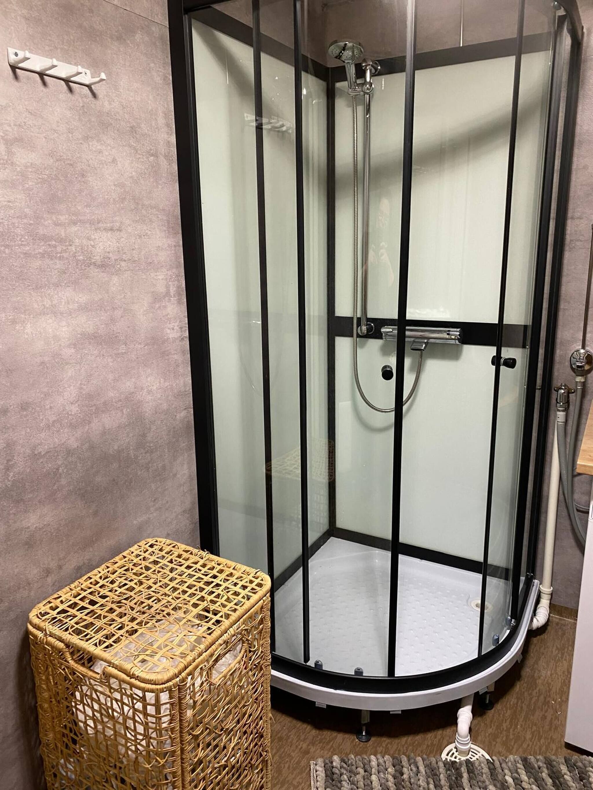 A glass-enclosed shower with a handheld showerhead, a small wicker basket, and a textured rug on the floor.