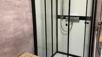 A glass-enclosed shower with a handheld showerhead, a small wicker basket, and a textured rug on the floor.
