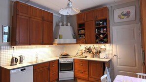 Ett kök med träskåp, en vit bänkskiva, en spis, en diskmaskin och en hängande lampa.