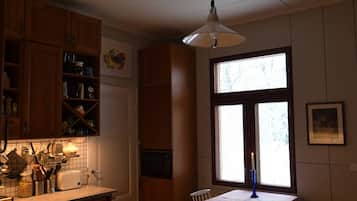 A kitchen with wooden cabinets, a dining table with chairs, a hanging light fixture, and a window with a candle.