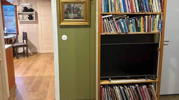 A room with a bookshelf filled with books, a television, a decorative mask on the wall, and a patterned rug on the floor.
