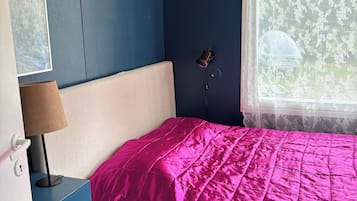 A bedroom with a bed, a nightstand, a lamp, a window with a curtain, and a wall with a decorative element.
