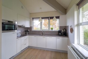 A modern kitchen with white cabinets, a built-in oven, a sink, and pendant lights above the window. - Elegant Waterfront Bungalow with Jetty (Makkum)