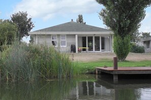 A house with a covered porch, a pond in front, and a duck on the dock. - Elegant Waterfront Bungalow with Jetty (Makkum)