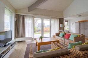 Ein modernes Wohnzimmer mit Flachbildfernseher, einer Sofagarnitur, einem Couchtisch und einem Korbstuhl.