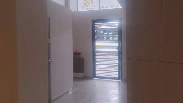 Un couloir doté d’un sol carrelé, une porte sur la gauche et une fenêtre avec des stores sur la droite.