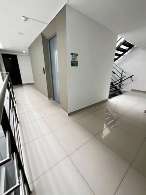 A clean, modern hallway with a metal railing, a door, and a staircase with a black railing. - VIP Nomad Nest in New PH with Air C, Kitchen, steps to Metroplus (Medellín)