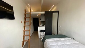 Une petite chambre à coucher comprenant un lit, une échelle en bois, un bureau et un téléviseur.