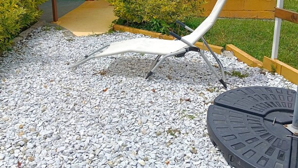 A covered outdoor seating area with a white lounge chair, gravel ground, and a view of a green hillside. - Nomad Nest near Guatapé Jacuzzi Turkish WiFi-full (El Peñol)