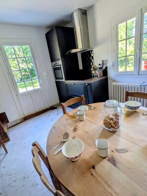 A dining area with a round wooden table, chairs, and a kitchen in the background.