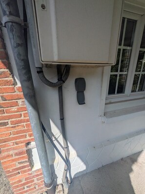 An outdoor electrical box attached to a brick wall with a window nearby.