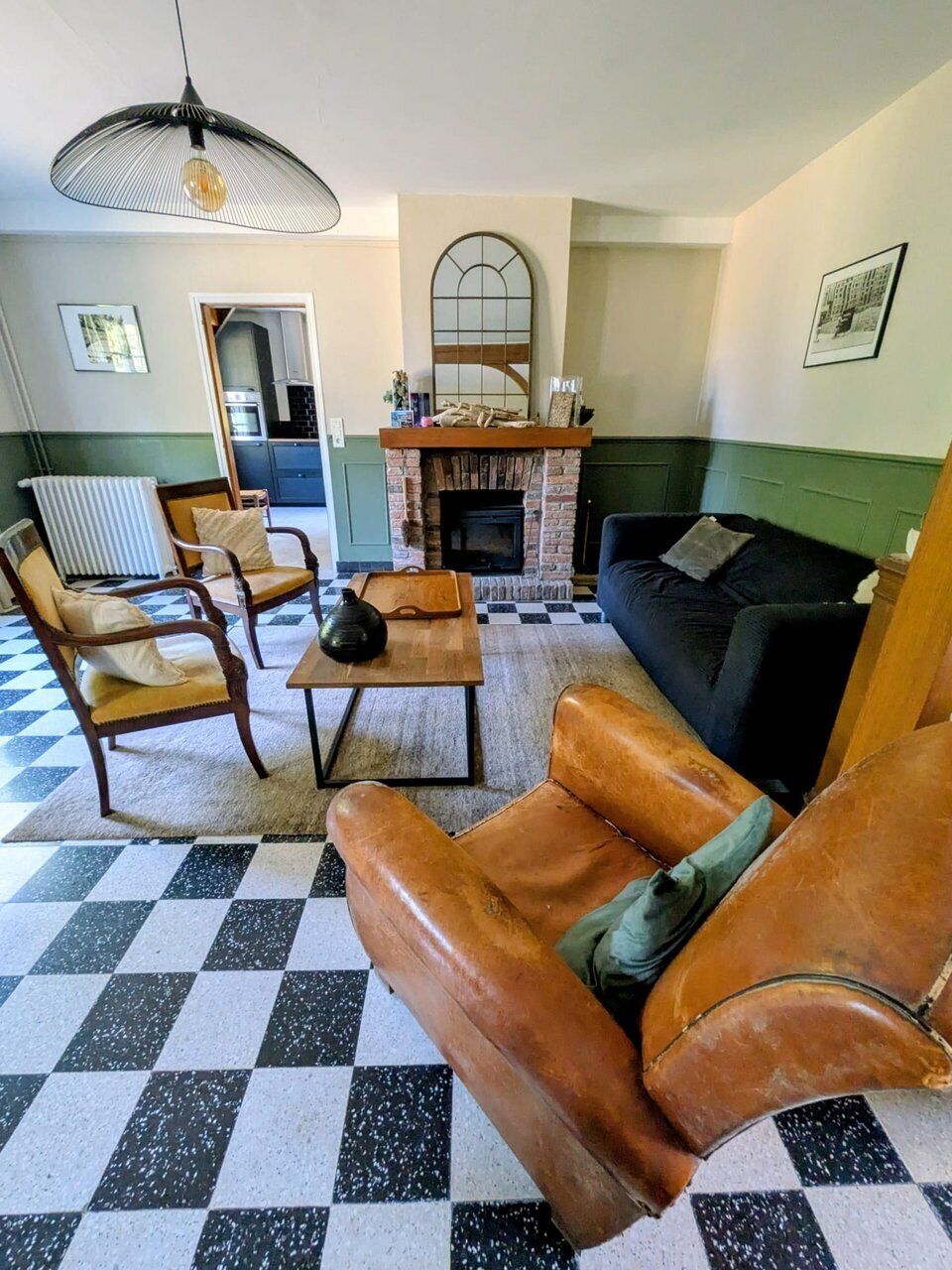 Een woonkamer met een geruit vloerkleed, leren fauteuils, een bank, een open haard en een hanglamp.