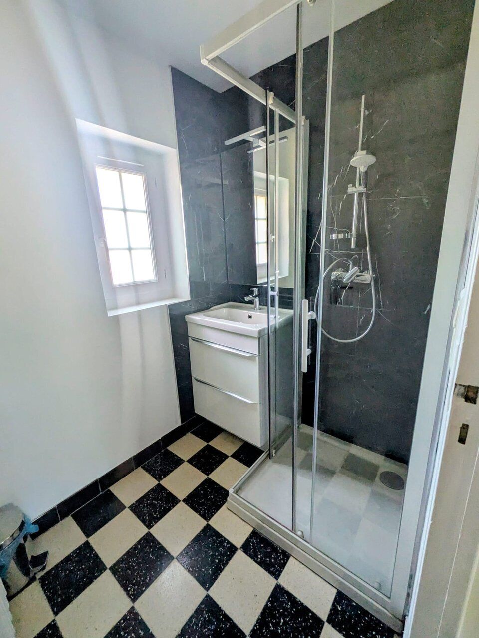 A bathroom with a glass shower enclosure, a sink, and a mirror.