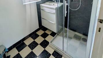 A bathroom with a glass shower enclosure, a sink, and a mirror.