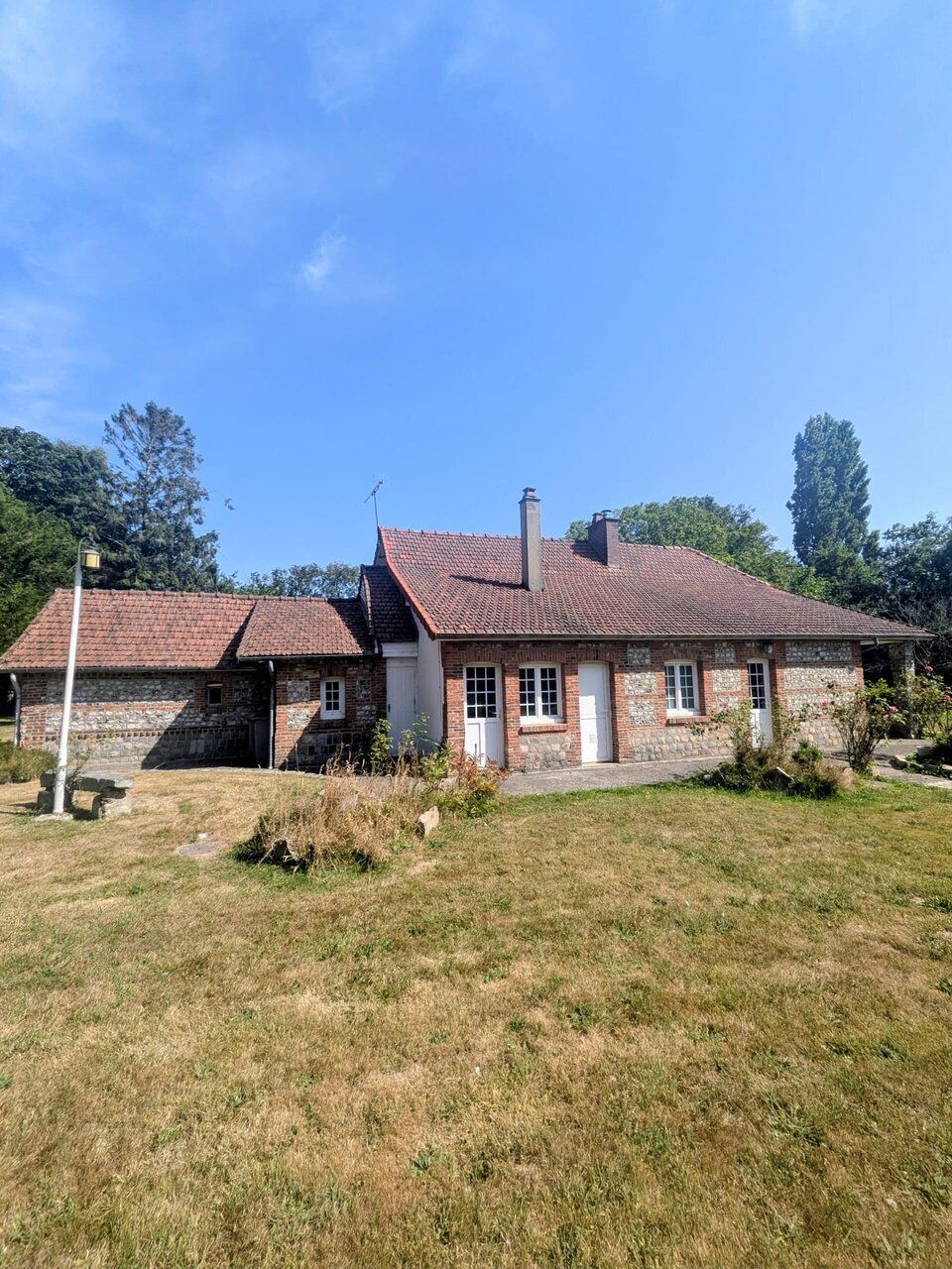 Ein zweistöckiges Steinhaus mit rotem Ziegeldach, Schornstein und einem kleinen Garten.