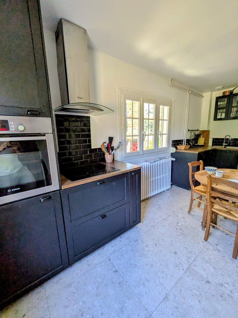 A modern kitchen with a built-in oven, a stove, and a range hood. There is a window with a view of greenery outside.