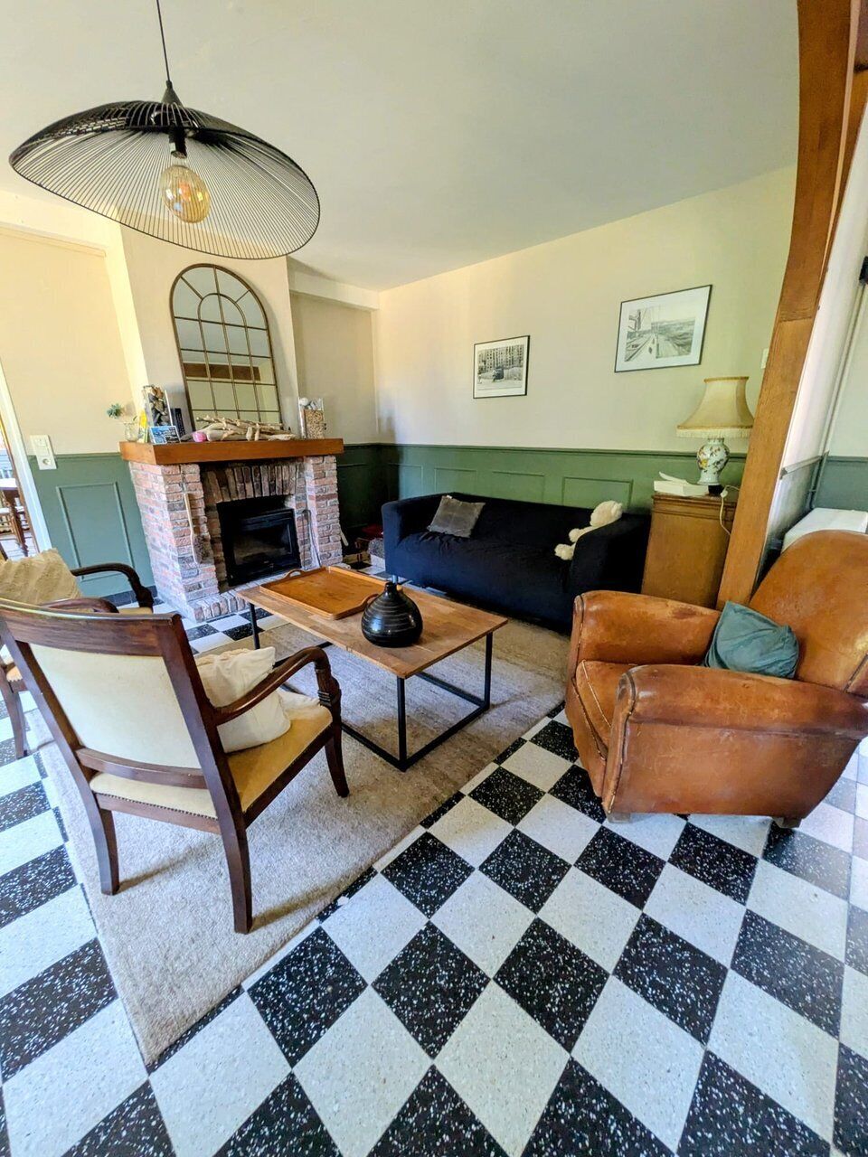 A living room with a checkered floor, a fireplace, a sofa, a leather armchair, and a hanging light fixture.