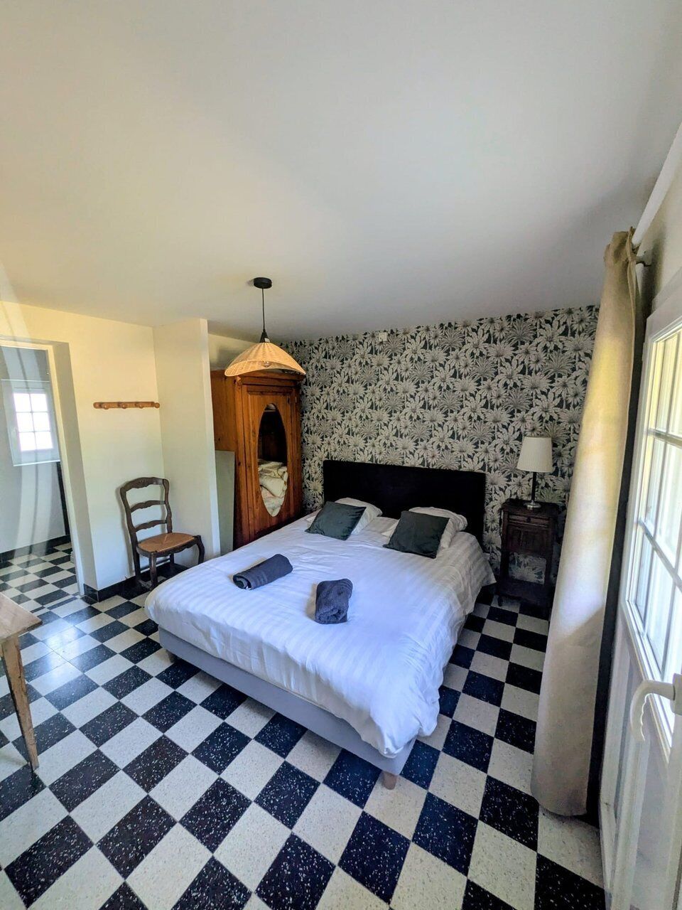 A hotel room with a checkered floor, a bed with white bedding, a wooden wardrobe, and a small table.