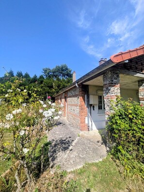 A house with a stone facade, a red roof, and a garden with white flowers.