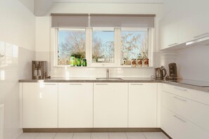 A modern kitchen with white cabinets, a stainless steel sink, and a window with a view of trees. - Comfortable Bungalow Stay by the Water (Makkum)