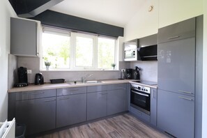 Une cuisine moderne avec des meubles gris, un four encastré, un micro-ondes et une fenêtre donnant sur un espace verdoyant.