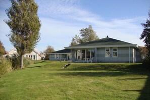 A two-story house with a covered porch, a grassy yard, and a tree. - Comfortable Bungalow Stay by the Water (Makkum)