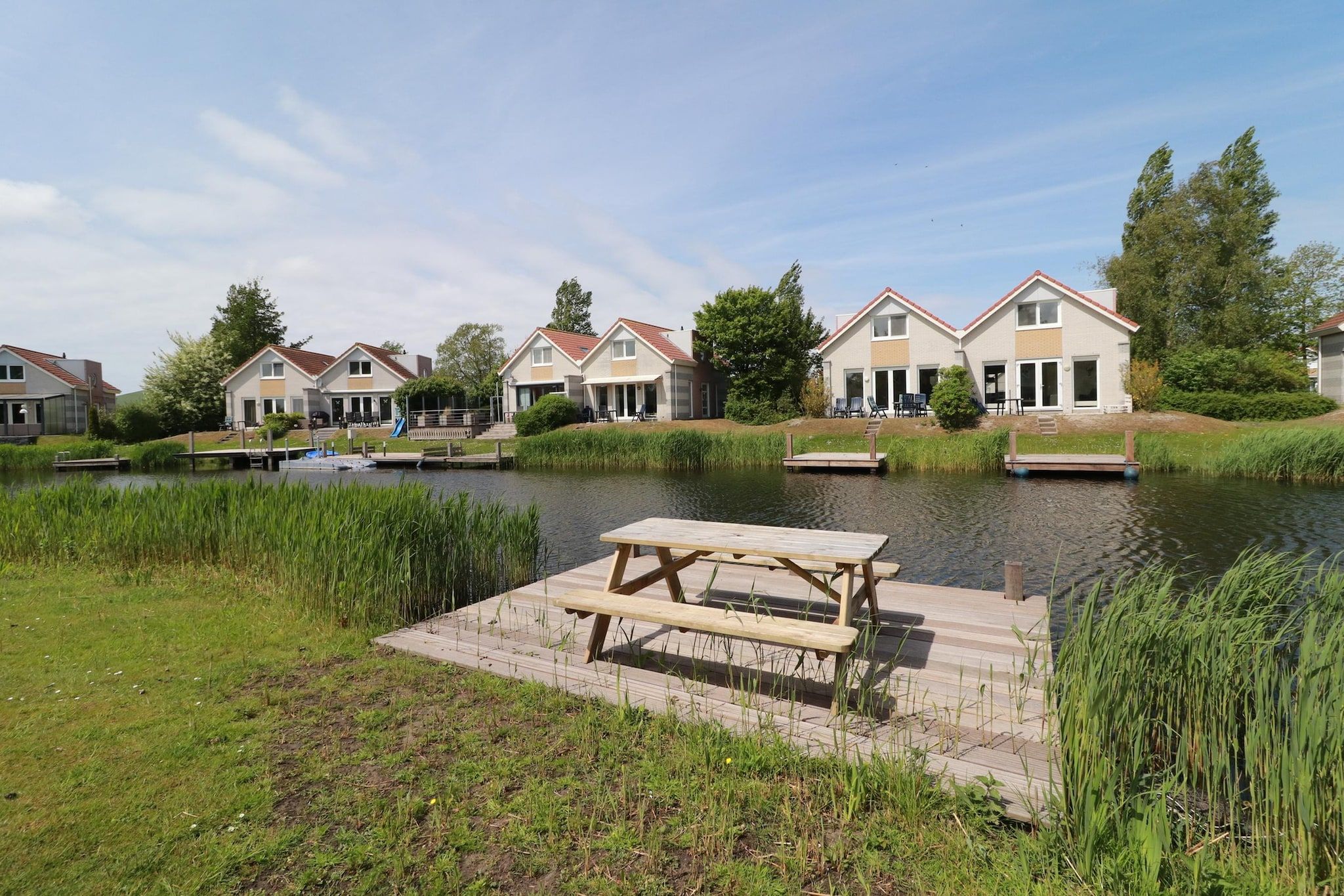 A lakeside property with a wooden dock and picnic table, surrounded by houses with red roofs.