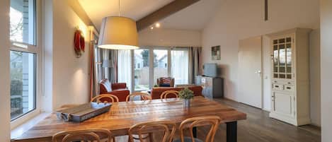 Un coin repas avec une table et des chaises en bois, une grande lampe suspendue et une vue sur l’extérieur par une fenêtre.