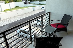Ein Balkon mit Metallgeländer, einem Glastisch und zwei Korbstühlen mit roten Kissen.