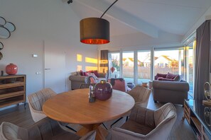 A modern living room with a round wooden table, leather chairs, a large window with a view, and a hanging pendant light. - Luxury 3BR Waterfront Villa (Makkum)
