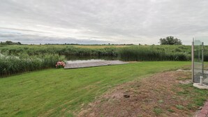 Eine Rasenfläche mit einem Teich, einer hölzernen Mole und einem Glasgebäude.
