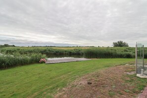 A grassy area with a pond, a wooden dock, and a glass structure. - Luxury 3BR Waterfront Villa (Makkum)