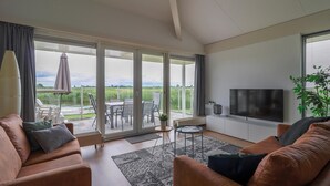 Ein modernes Wohnzimmer mit einer Couch, einem Fernseher und Blick auf eine Terrasse mit Gartenmöbeln.