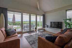 A modern living room with a sofa, TV, and a view of a patio with outdoor furniture. - Luxury 3BR Waterfront Villa (Makkum)