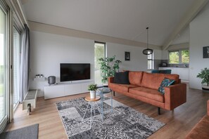 A modern living room with a sofa, a TV, a small table, and a large window. - Luxury 3BR Waterfront Villa (Makkum)