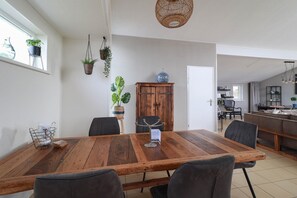 Een eetgedeelte met een grote houten tafel, vier stoelen en een kastje met een glazen object erop.