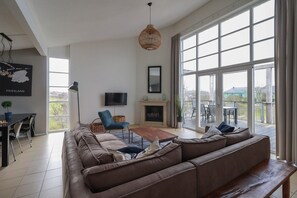 Un salon moderne doté d’un grand canapé d’angle, d’un téléviseur à écran plat, d’une cheminée et d’un balcon avec un espace salon extérieur.