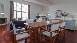 Ein geräumiger Wohnbereich mit einem Holzessttisch, weißen Stühlen, einer Couch und einer Küche im Hintergrund.